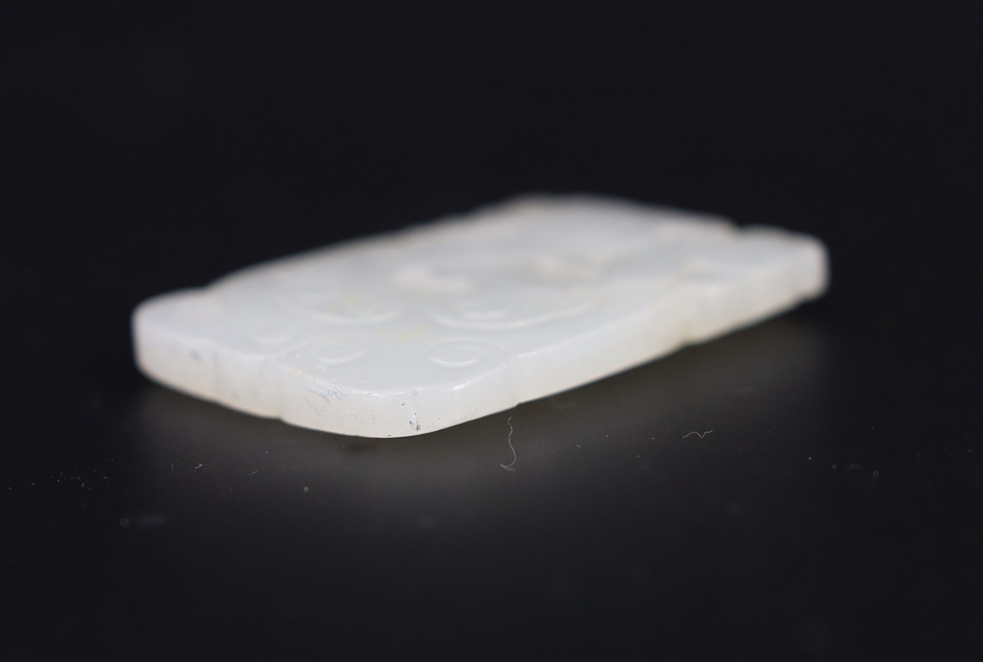 A Chinese white jade plaque, 19th century, 4.9cm, splinter chip, wood stand